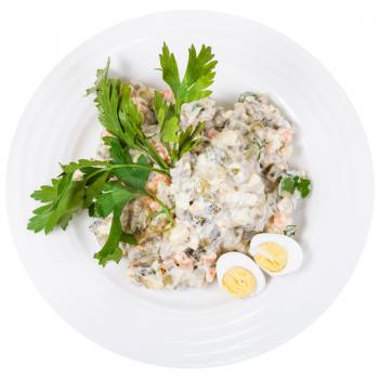 top view of olivier russian salad with mayonnaise decorated with green parsley and boiled eggs on white plate isolated on white background