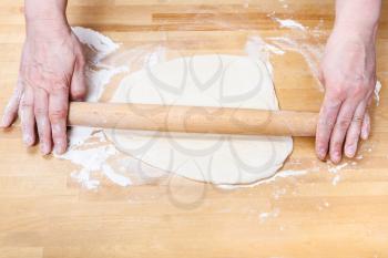 female hands roll out the dough with a rolling pin on wooden table