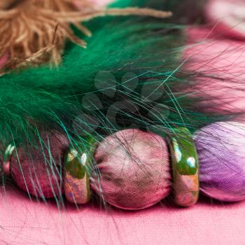 detail of handmade textile necklace - violet painted silk batik bead and green ceramic rings with green feather close up on pink background