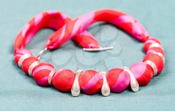 textile necklace from red silk balls and silver rings on green background