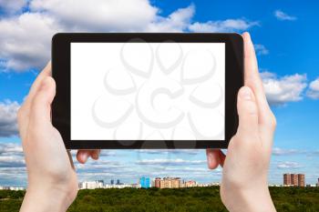 season concept - tourist photographs blue sky with white clouds over city and green trees on tablet pc with cut out screen with blank place for advertising