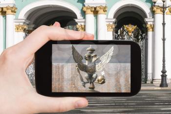 travel concept - tourist photographs Double-headed eagle symbol of Russian Empire on gate of Winter Palace in Saint Petersburg, Russia on smartphone