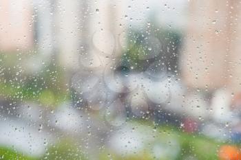 raindrops on window glass and blurred residential quarter on background