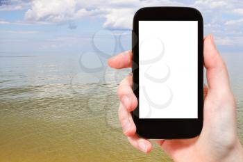 travel concept - tourist photographs of calm water of Azov Sea on smartphone with cut out screen with blank place for advertising