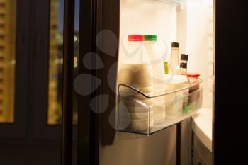 Open door of home fridge with dairy products in night