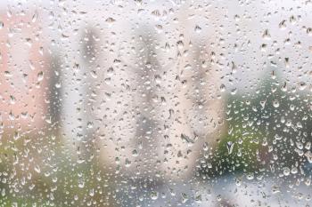 rainy weather in city - view of rain drops on window pane of urban house