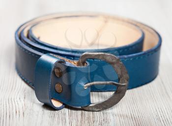 hand made blue leather belt with forged buckle on wooden table