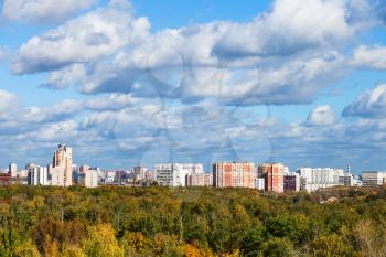 autumn landscape with yellow and green forest and blue sky with white clouds over city in sunny autumn day