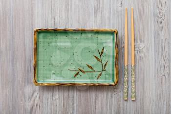 top view of one green square plate and chopsticks on gray brown table