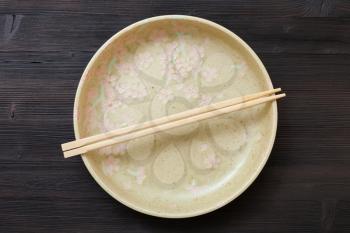 top view of one yellow green plate with chopsticks on dark brown board