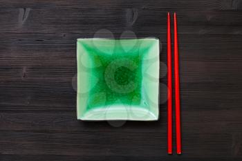 top view of one green square saucer with red chopsticks on dark brown board