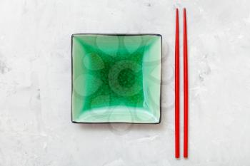 top view of green square saucer and red chopsticks on gray concrete board