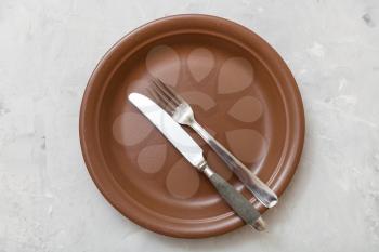 food concept - top view of brown plate with parallel knife, spoon on gray concrete surface