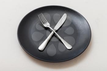 food concept - black plate with crossing knife, spoon on white plastering board