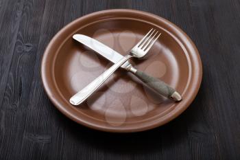 food concept - brown plate with crossing knife, spoon on dark brown table