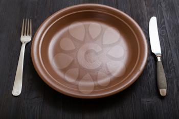 food concept - brown plate with knife, spoon on dark brown table