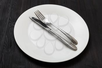 food concept - white plate with parallel knife, spoon on dark brown table