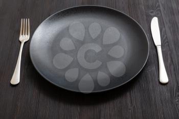 food concept - black plate with knife, spoon on dark brown table
