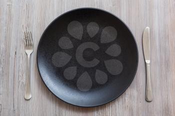 food concept - top view of black plate with knife, spoon on gray brown table