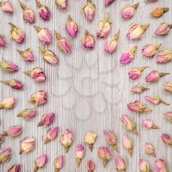 round frame from dried pink rose flower buds on wooden plank