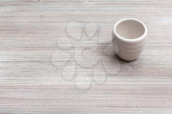 food concept - white ceramic cup for sake (ochoko, choko) on gray brown wooden board