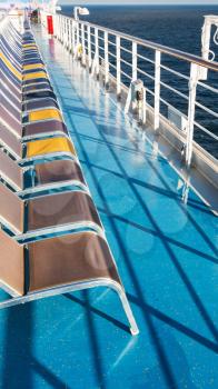 line of empty sunbathing chairs on deck of cruise liner