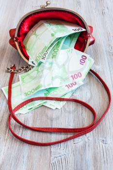 100 euro banknotes fall out from red leather handbag on wooden table