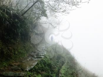 travel to China - man at wet pathway on hill slope in rainy misty spring day in area of Dazhai Longsheng Rice Terraces (Dragon's Backbone terrace, Longji Rice Terraces)