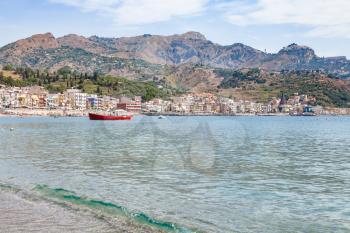 travel to Sicily, Italy - boat in Ionian sea near waterfront of Giardini Naxos town and view of Taormina city on cape in summer