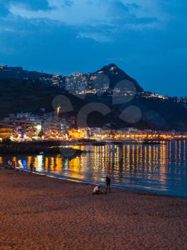 travel to Sicily, Italy - view urban beach in Giardini Naxos town and view of Taormina city on cape in summer night