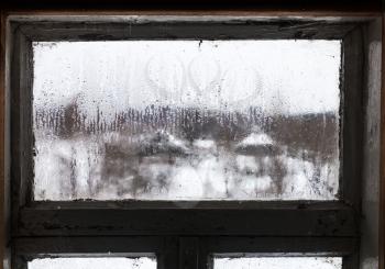 blurry view of russian village through misted frozen window of rural house in cold winter day (focus on ice surface on the glass)