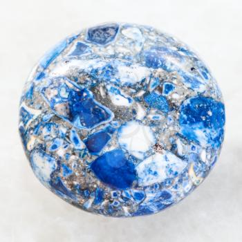 macro shooting of mineral rock specimen - cabochon from artificial pressed Lazurite stone on white marble background