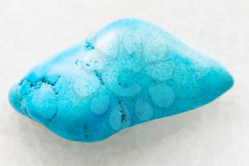 macro shooting of natural mineral rock specimen - tumbled Turquenite (blue howlite) gemstone on white marble background