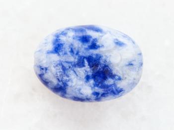 macro shooting of natural mineral rock specimen - bead from Lapis lazuli gemstone on white marble background
