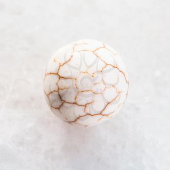 macro shooting of natural mineral rock specimen - ball from cracked Cacholong (milky white opal, Kalmuck agate, pearl opal) gemstone on white marble background