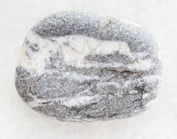 macro shooting of natural mineral rock specimen - tumbled gray Gneiss pebble on white marble background
