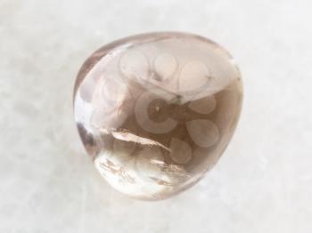 macro shooting of natural mineral rock specimen - tumbled smoky quartz gem stone on white marble background