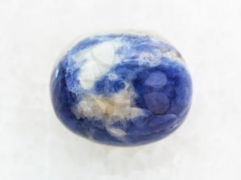 macro shooting of natural mineral rock specimen - tumbled Sodalite gem stone on white marble background