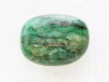 macro shooting of natural mineral rock specimen - tumbled green beryl gemstone on white marble background