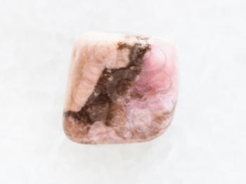 macro shooting of natural mineral rock specimen - tumbled Rhodochrosite gemstone on white marble background