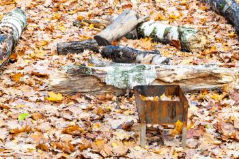 forgotten small barbecue grill with trash on meadow covered by fallen leaves in city park in autumn