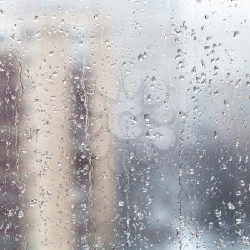 urban background - raindrops on home window glass (focus on water trickles on windowpane) in winter season