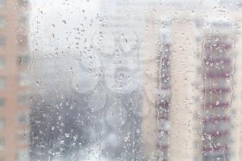 urban background - drops of melting snow on window glass (focus on water trickles on windowpane) in winter season