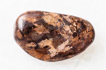 macro shooting of natural mineral rock specimen - tumbled Bronzite gemstone on white marble background from Peru