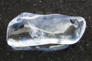macro shooting of natural mineral rock specimen - tumbled clear Quartz (rock-crystal) gemstone on dark granite background