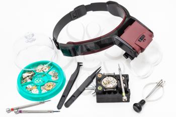 watchmaker workshop - various tools with head-mounted magnifier and spare parts for repairing mechanical watch on white background