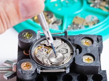 watchmaker workshop - repairing of old wristwatch in holder with screwdriver close up
