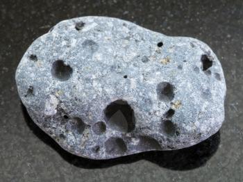macro shooting of natural mineral rock specimen - pebble of gray pumice stone on dark granite background from Sicily