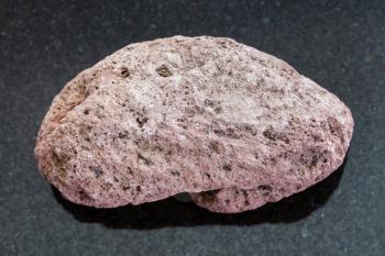 macro shooting of natural mineral rock specimen - red pumice pebble on dark granite background from Sicily