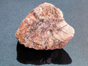 macro shooting of natural mineral rock specimen - rough pink Granite stone on dark granite background